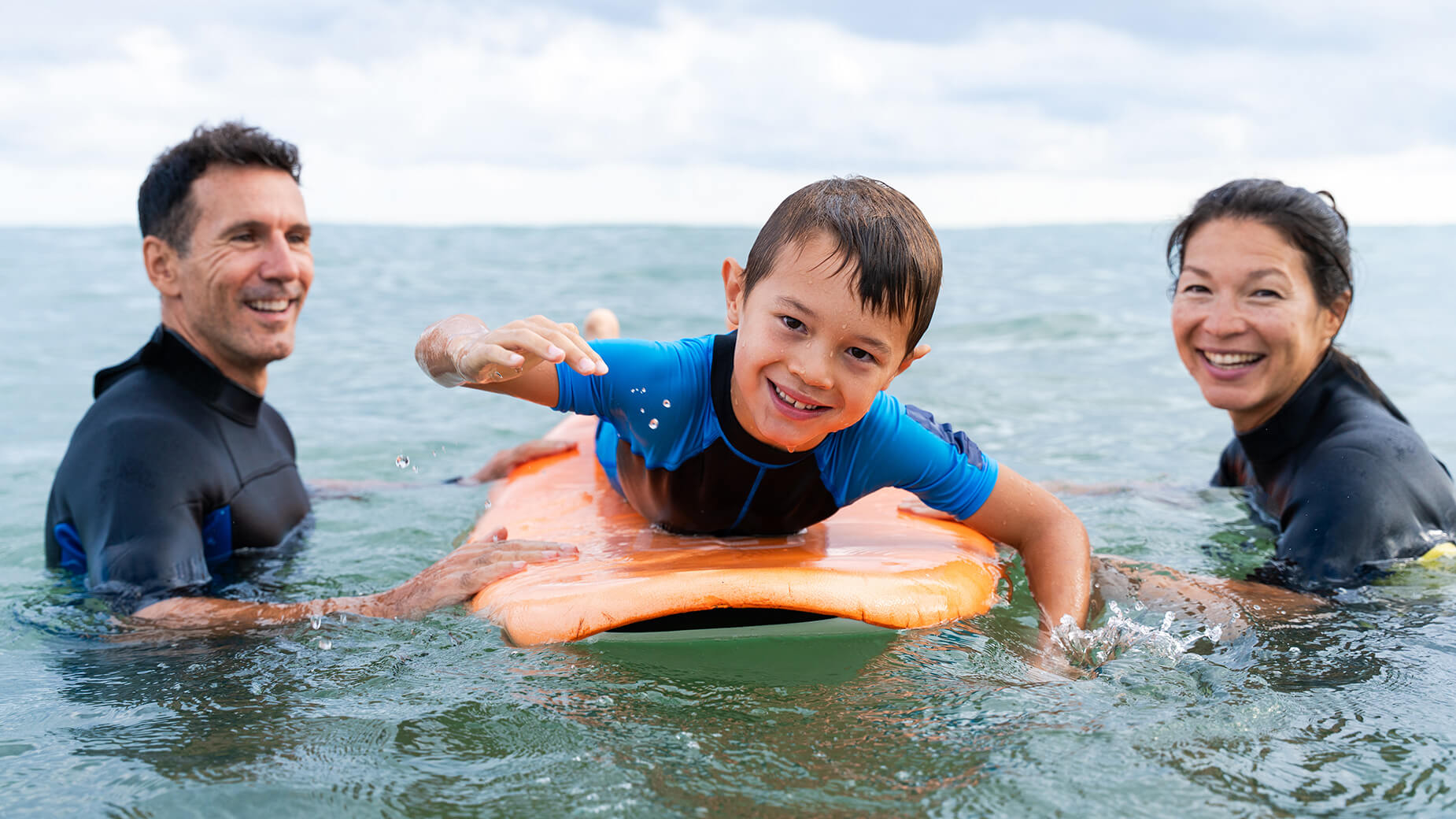 young boy on surf board with his parents