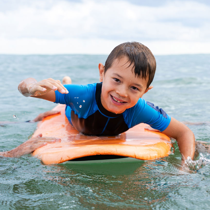 young boy on surf board with his parents
